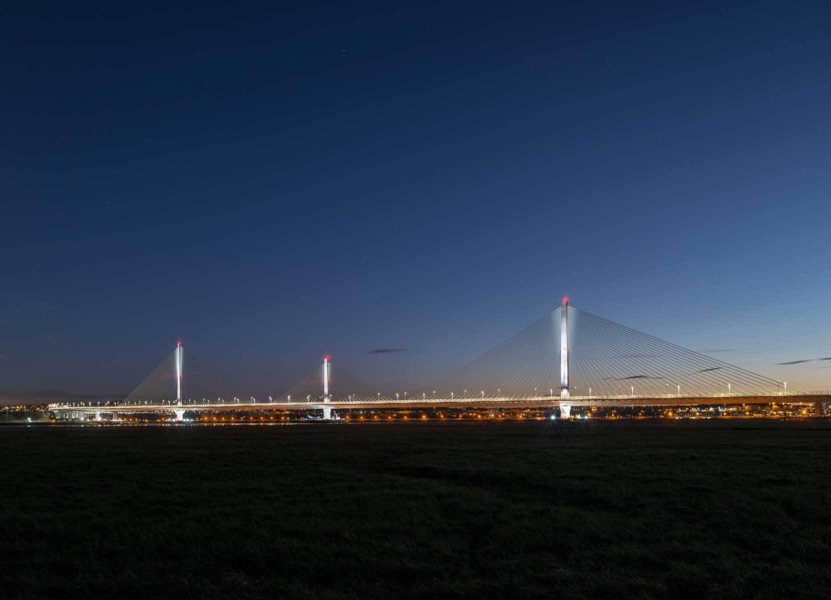 A large modern suspension bridge with three pillars seen at night from a distance