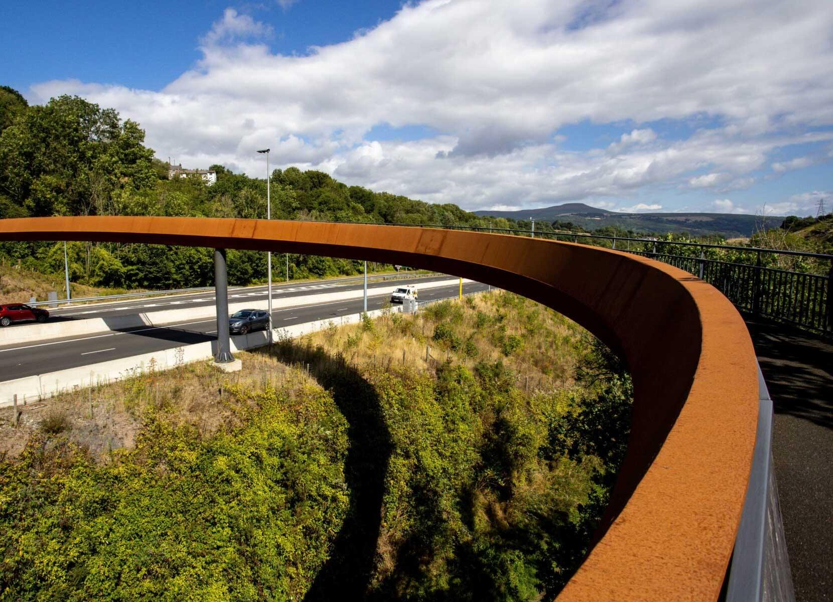  A footbridge swooping in a curve over a busy dual carriageway.