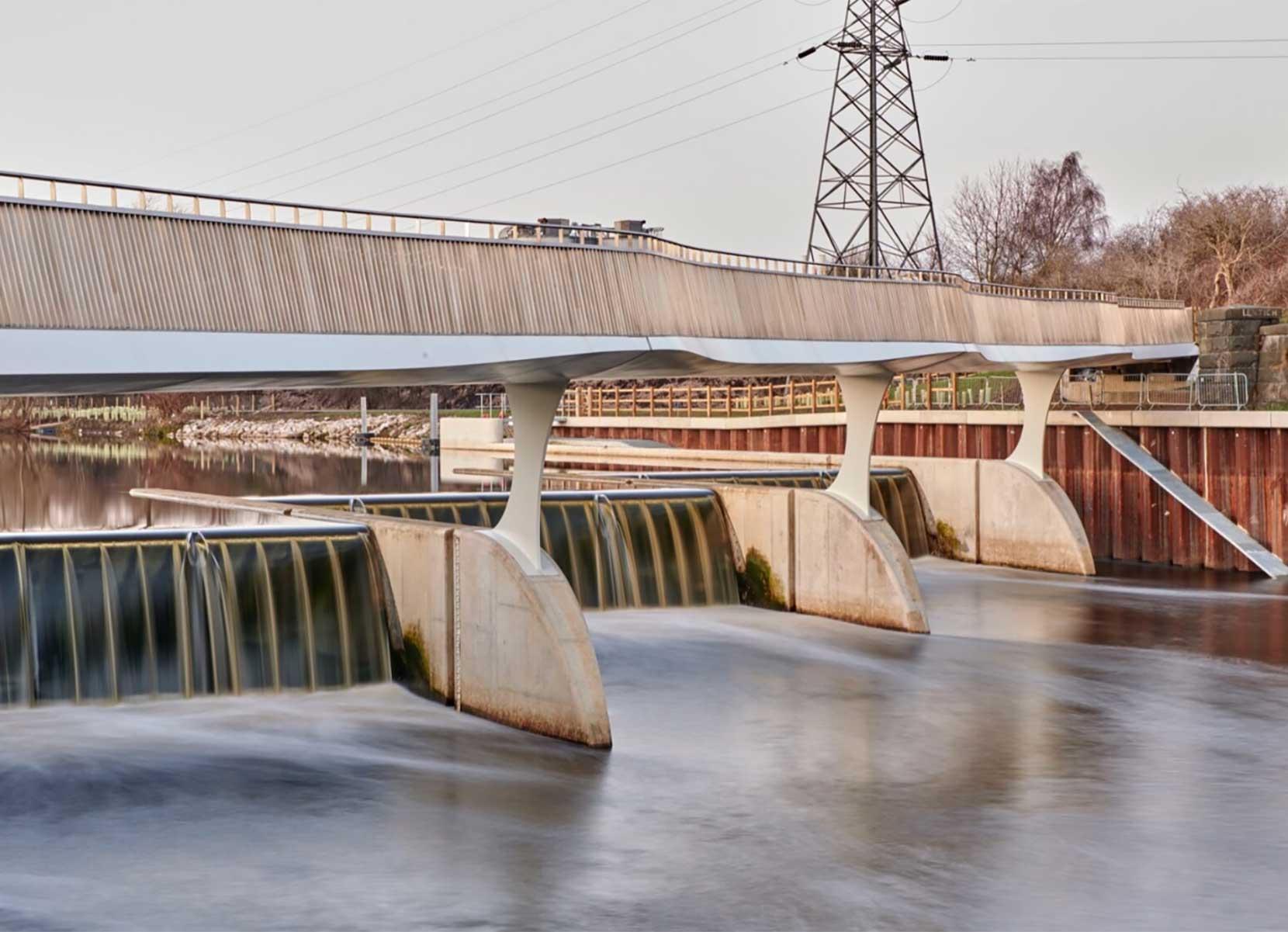 An elegantly curved footbridge suspended on three stilts spanning a weir.