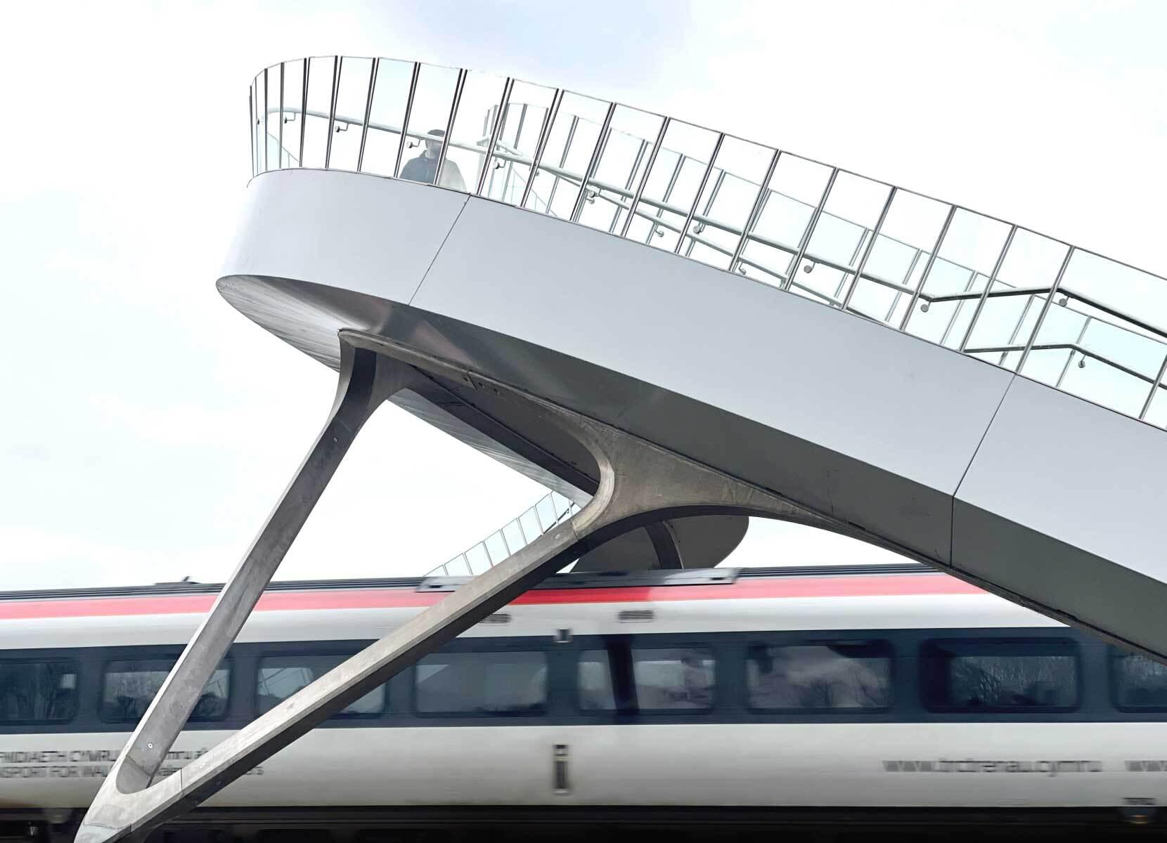 A modern footbridge spans a rail track as a train passes underneath