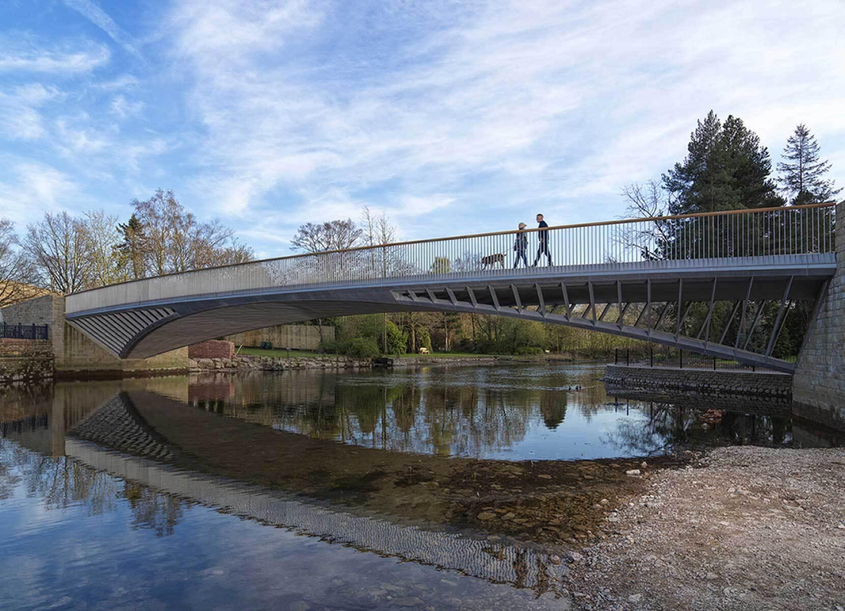 Two people walk a dog over an modern and elegant bridge spanning a calm river