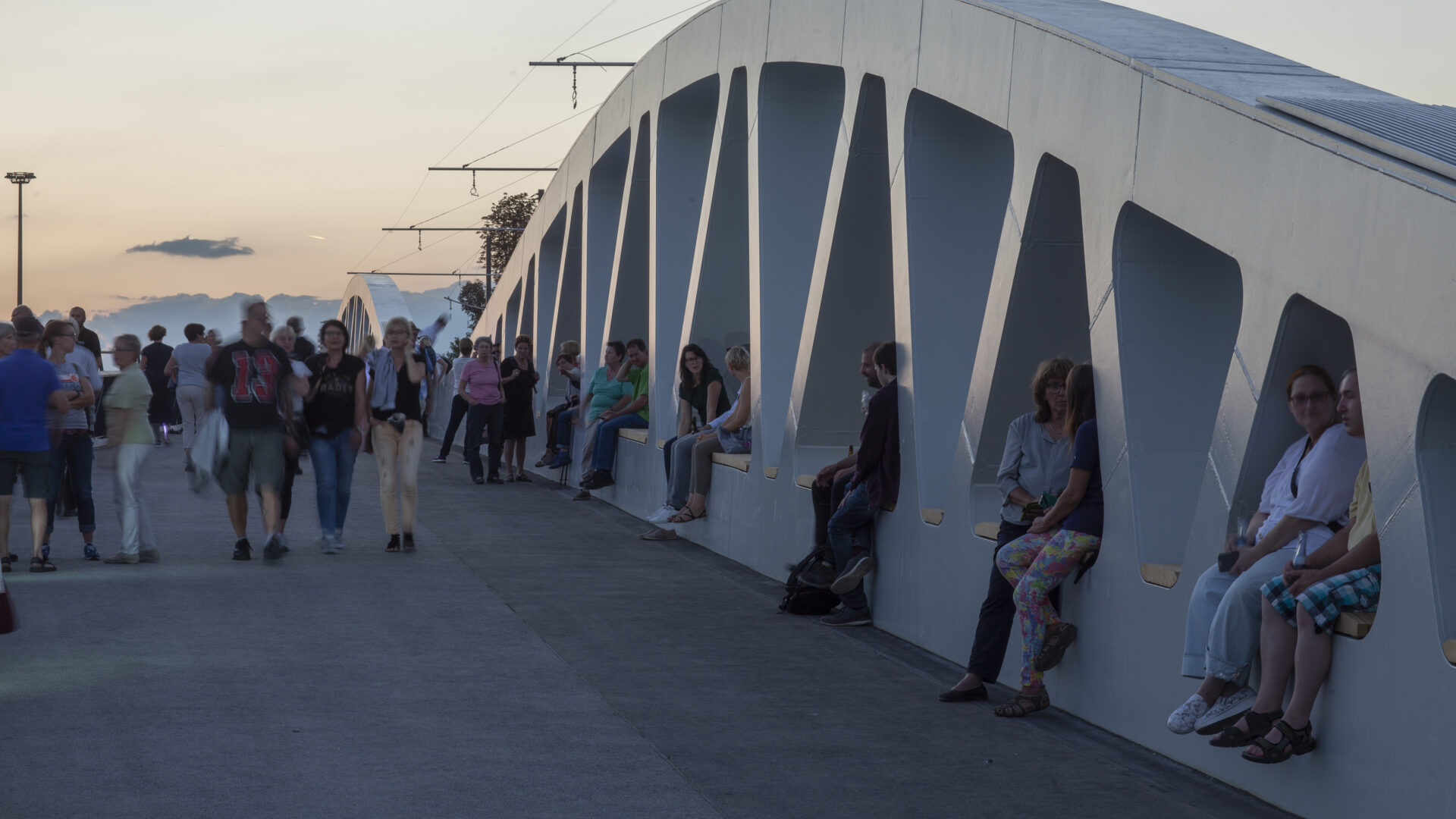 People and walking and sitting on Kienlesberg bridge with sunset backdrop