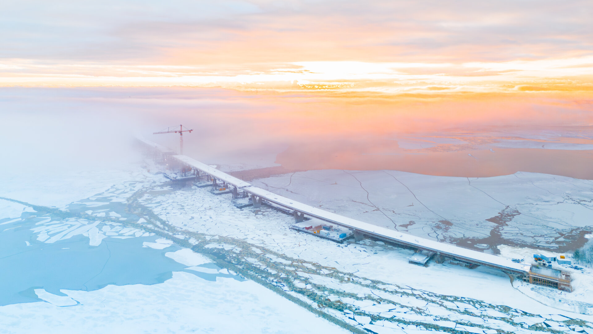 A bridge stretches into the distance with sunset above and blue ice and snow below
